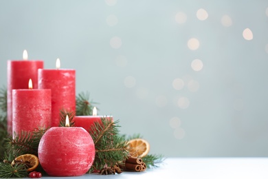 Photo of Burning red candles with Christmas decor on table against blurred lights. Space for text
