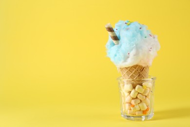 Photo of Sweet cotton candy in waffle cone on yellow background. Space for text