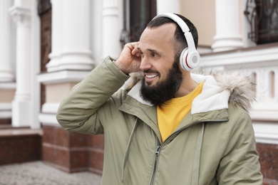 Photo of Mature man with headphones listening to music outdoors. Space for text