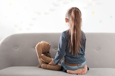 Photo of Lonely little girl with toy sitting on couch indoors. Autism concept