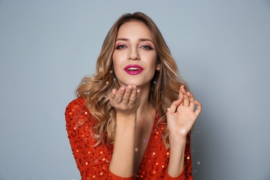 Photo of Happy woman blowing glitter on grey background. Christmas party