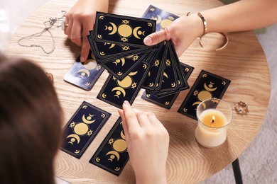 Photo of Woman pulling one tarot card at table indoors, closeup. Fortune telling