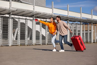 Photo of Being late. Couple with red suitcase running outdoors, space for text
