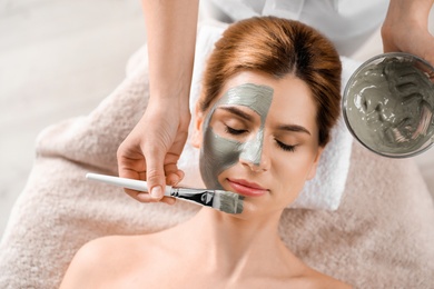 Photo of Cosmetologist applying mask onto woman's face in spa salon, top view