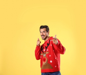 Photo of Portrait of happy young man in Christmas sweater on yellow background