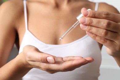 Photo of Woman applying cosmetic serum onto her hand on blurred background, closeup