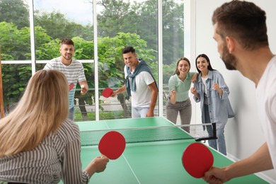 Photo of Happy friends playing ping pong together indoors
