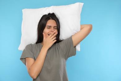 Photo of Sleepy young woman with soft pillow yawning on light blue background