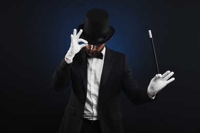 Photo of Magician in top hat holding wand on black background