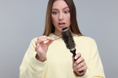 Photo of Woman untangling her lost hair from brush on light grey background, selective focus. Alopecia problem