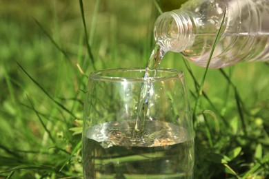 Photo of Woman pouring pure water into glass outdoors on sunny day, closeup