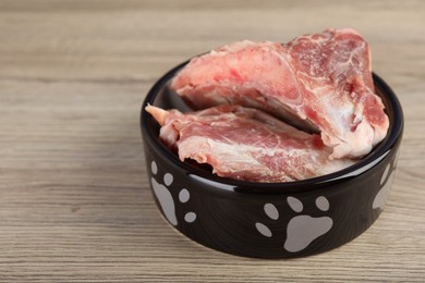 Photo of Feeding bowl with raw meaty bones on wooden table. Natural animal food