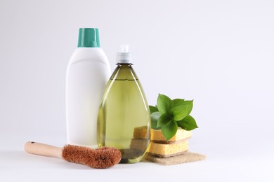 Photo of Bottles of cleaning product, brush, sponges and floral decor on white background