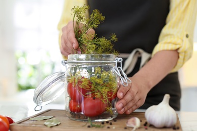 Photo of Woman putting dill into pickling jar at table in kitchen, closeup