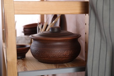 Photo of Clay dishes and crafting tools on wooden rack in workshop, closeup