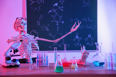 Skeleton and different chemistry glassware in classroom, toned in pink
