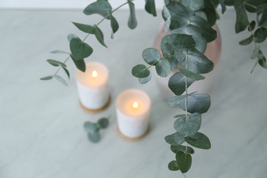 Photo of Beautiful eucalyptus branches and burning candles on grey table, closeup. Interior element