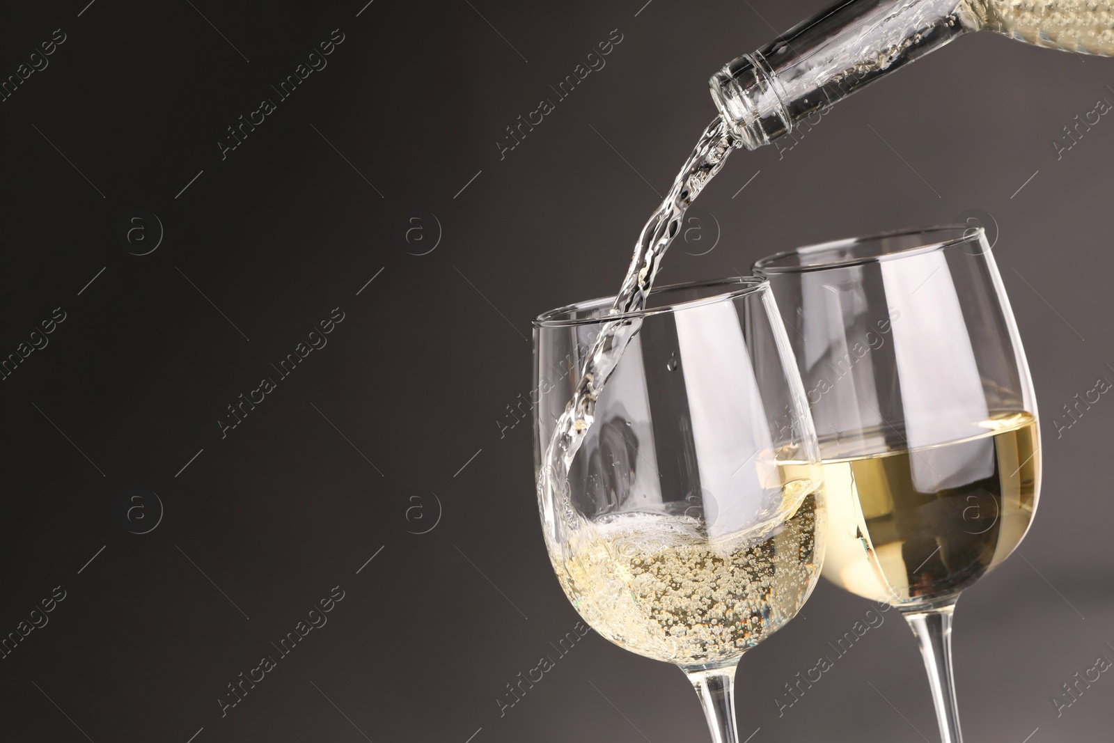 Photo of Pouring white wine into glass against grey background, closeup. Space for text