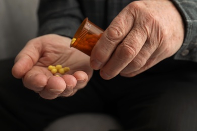Photo of Senior man pouring pills from bottle into hand, closeup