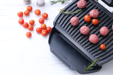 Photo of Electric grill with meatballs, tomatoes and rosemary on white table, above view. Space for text