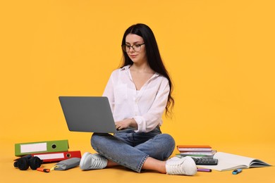 Photo of Student with laptop sitting among books and stationery on yellow background