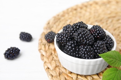 Photo of Bowl of tasty blackberries with leaves on white wooden table, space for text
