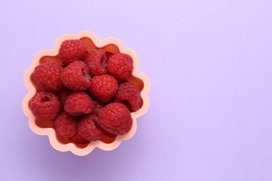 Photo of Bowl of fresh delicious raspberries on violet background, top view. Space for text