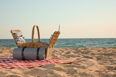 Photo of Blanket with picnic basket on sandy beach near sea, space for text