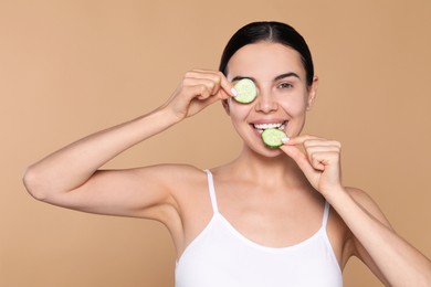 Photo of Beautiful young woman with slices of cucumber on beige background