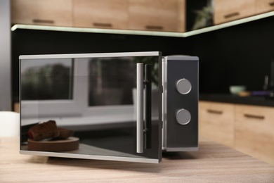 Photo of Open modern microwave oven on table in kitchen