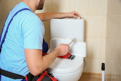 Photo of Plumber repairing toilet with wrench indoors, closeup