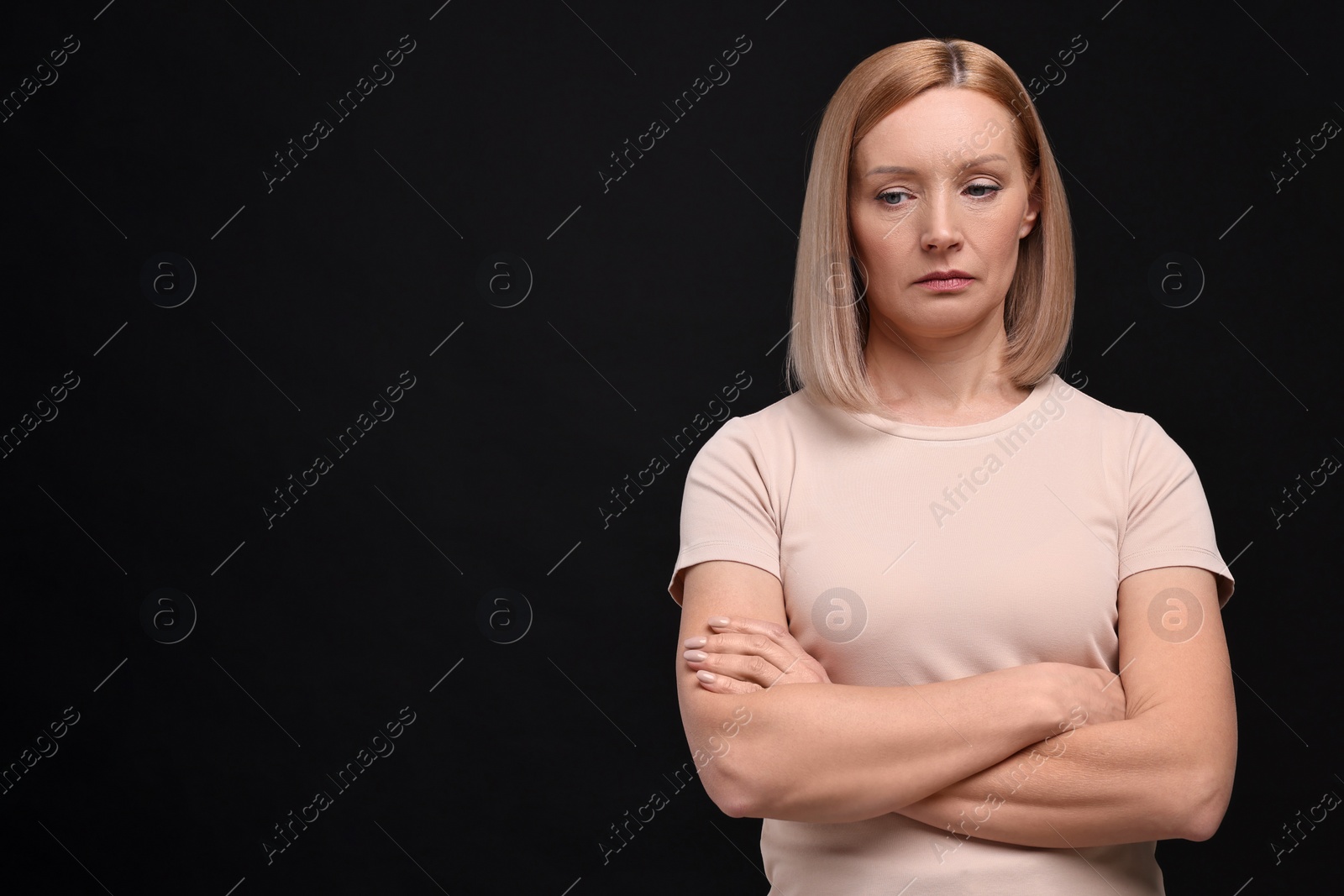 Photo of Portrait of sad woman with crossed arms on black background. Space for text