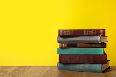 Photo of Stack of old hardcover books on wooden table against yellow background, space for text
