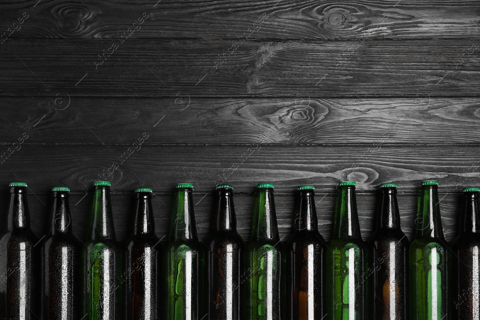 Photo of Glass bottles of beer on black wooden background, flat lay. Space for text