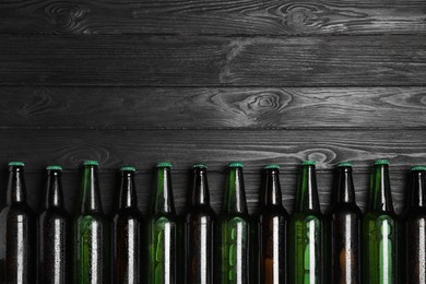 Glass bottles of beer on black wooden background, flat lay. Space for text