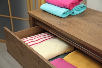 Wooden chest of drawers with different folded clothes indoors, closeup