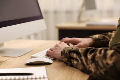 Military service. Soldier working with computer at wooden table in office, closeup