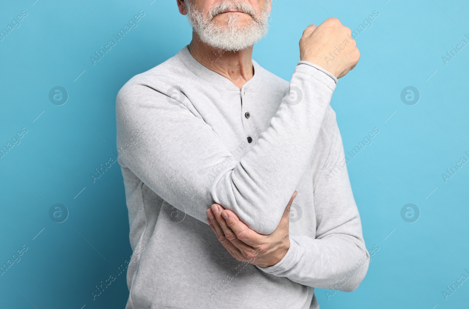 Photo of Arthritis symptoms. Man suffering from pain in elbow on light blue background, closeup