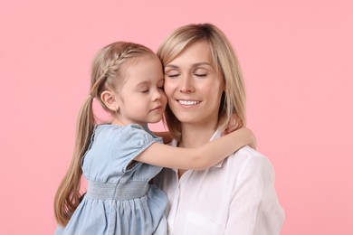 Daughter hugging her happy mother on pink background