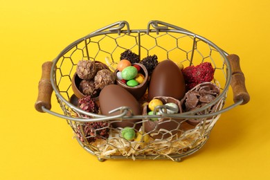 Photo of Basket with chocolate eggs and candies on yellow background