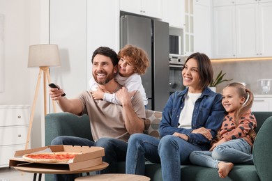 Photo of Happy family watching TV with pizza on sofa at home