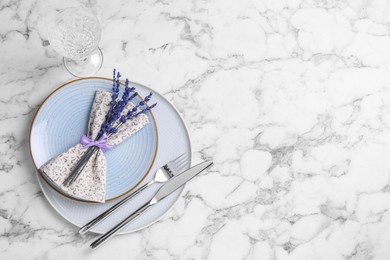Photo of Cutlery, napkin, plates, glass and preserved lavender flowers on white marble table, flat lay. Space for text