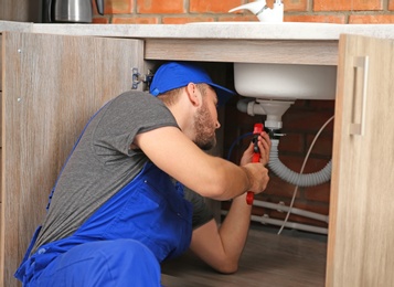 Photo of Professional plumber in uniform fixing sink indoors
