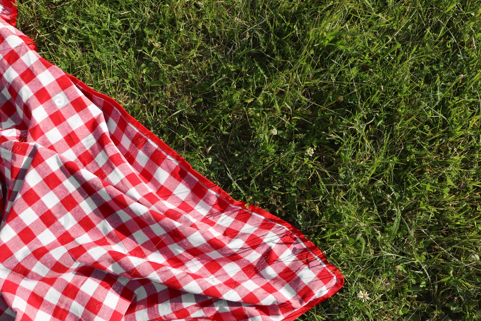 Photo of Checkered picnic tablecloth on fresh green grass, top view. Space for text