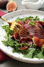 Photo of Eating tasty bresaola salad with fork at table, closeup