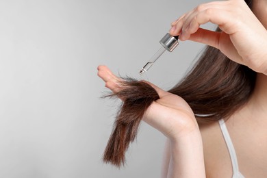 Photo of Woman applying essential oil onto hair on light grey background, closeup