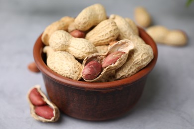 Photo of Fresh unpeeled peanuts in bowl on grey table, closeup