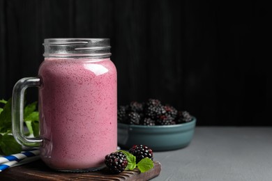 Photo of Mason jar of blackberry smoothie and berries on grey table. Space for text
