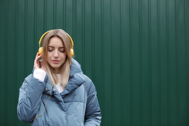 Photo of Young woman with headphones listening to music near color wall. Space for text