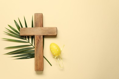 Photo of Wooden cross, painted Easter egg and palm leaf on beige background, top view. Space for text